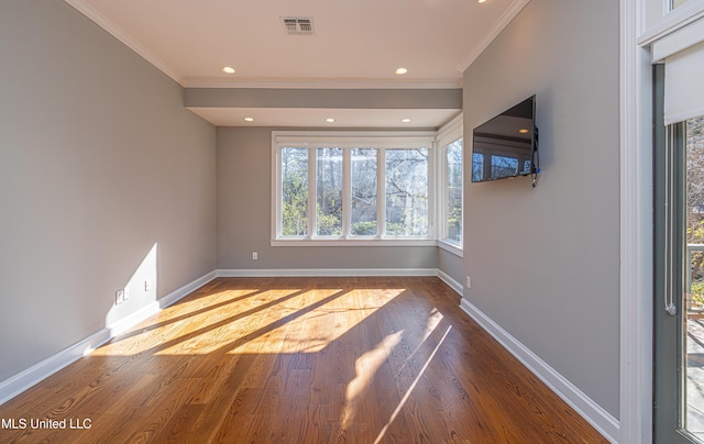 spare room featuring crown molding, wood finished floors, visible vents, and baseboards