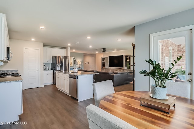 kitchen with white cabinetry, a center island with sink, appliances with stainless steel finishes, dark hardwood / wood-style floors, and light stone counters