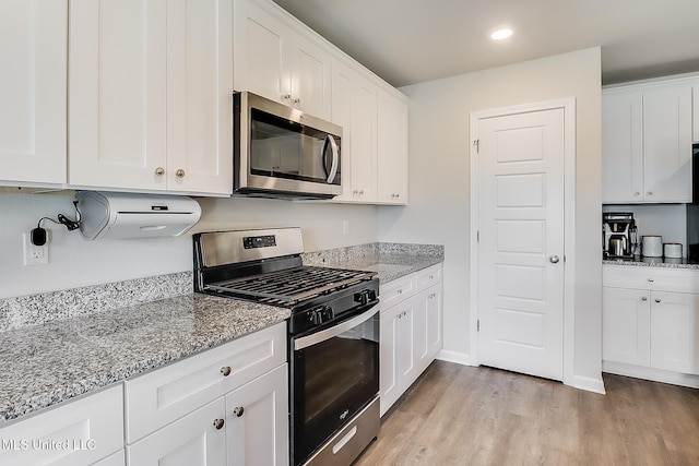 kitchen with stainless steel appliances, white cabinetry, and light stone counters