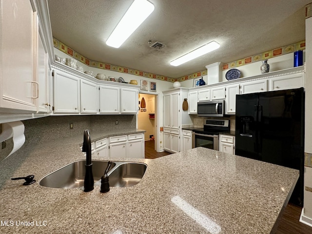 kitchen with sink, white cabinets, appliances with stainless steel finishes, light stone counters, and a textured ceiling