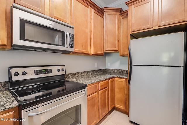 kitchen with dark stone countertops, ornamental molding, light tile patterned floors, and appliances with stainless steel finishes