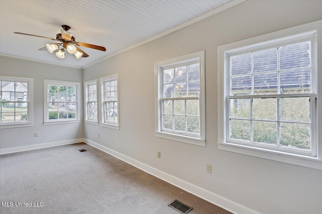 carpeted empty room with a wealth of natural light, baseboards, visible vents, and crown molding