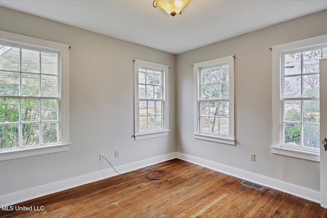 empty room featuring wood finished floors, visible vents, and baseboards