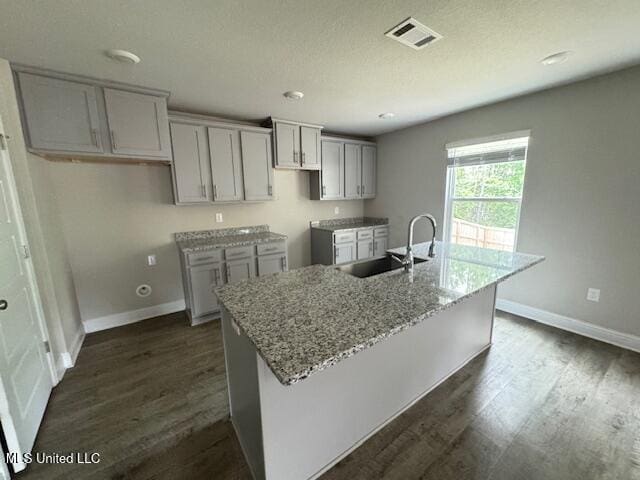 5378 Leeds Ln, Biloxi, MS 39532 - kitchen with a sink, a kitchen island with sink, light stone countertops, dark wood-type flooring, and baseboards