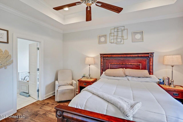 bedroom featuring a raised ceiling, ceiling fan, connected bathroom, crown molding, and light hardwood / wood-style flooring