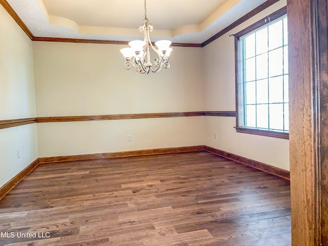 spare room with crown molding, a tray ceiling, a chandelier, and dark wood-type flooring