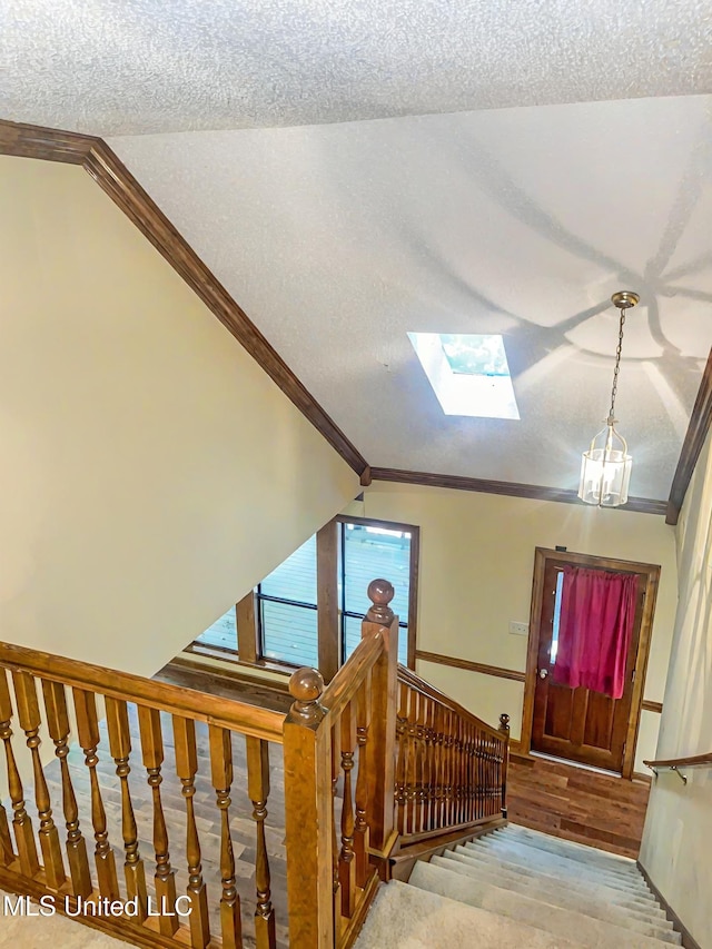 stairs featuring crown molding, lofted ceiling with skylight, a textured ceiling, and wood-type flooring