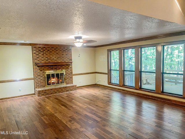 unfurnished living room with ceiling fan, a textured ceiling, wood-type flooring, a brick fireplace, and crown molding