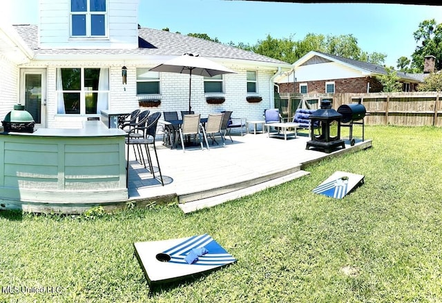 back of house with fence, a lawn, a wooden deck, brick siding, and roof with shingles