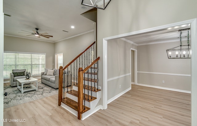 stairs with crown molding, hardwood / wood-style flooring, and ceiling fan with notable chandelier