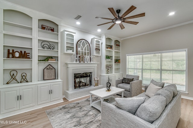 living room featuring crown molding, a brick fireplace, light wood-type flooring, and ceiling fan