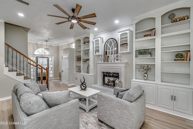 living room with built in features, light hardwood / wood-style flooring, a fireplace, and ceiling fan