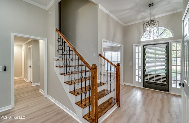 entryway with an inviting chandelier, ornamental molding, a high ceiling, and light wood-type flooring