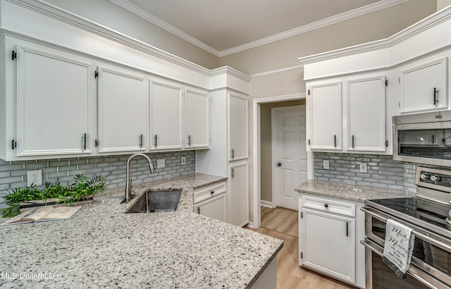 kitchen featuring tasteful backsplash, appliances with stainless steel finishes, white cabinetry, light hardwood / wood-style flooring, and sink