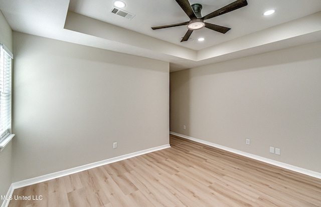 empty room with ceiling fan, a tray ceiling, and light wood-type flooring