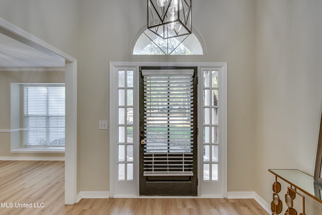 foyer with light hardwood / wood-style flooring, a notable chandelier, plenty of natural light, and crown molding