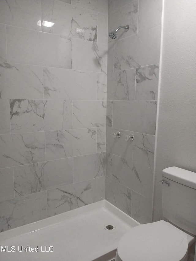 bathroom with a tile shower and toilet