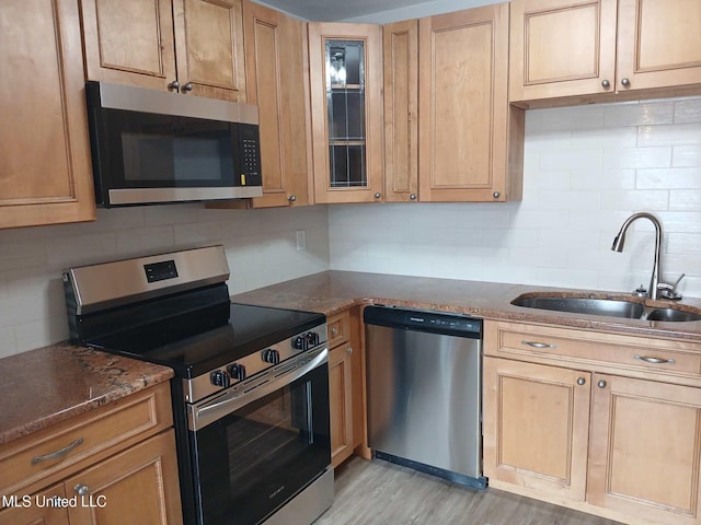 kitchen with sink, tasteful backsplash, light hardwood / wood-style flooring, dark stone counters, and stainless steel appliances