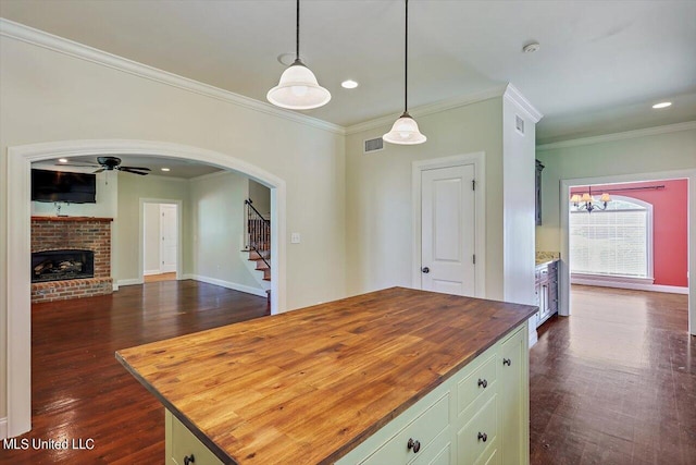 kitchen featuring ornamental molding, dark hardwood / wood-style floors, pendant lighting, wooden counters, and a center island