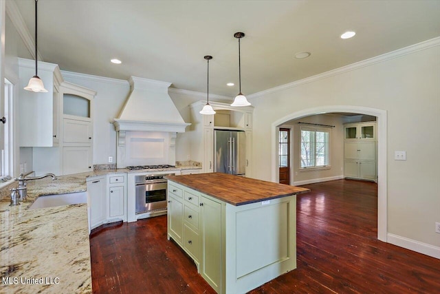 kitchen featuring dark hardwood / wood-style floors, custom range hood, wood counters, a center island, and appliances with stainless steel finishes