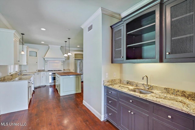 kitchen with white cabinets, hanging light fixtures, wood counters, custom range hood, and sink