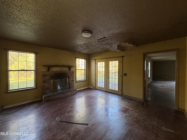 unfurnished living room with french doors, a healthy amount of sunlight, a textured ceiling, and a brick fireplace