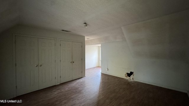 unfurnished bedroom featuring a textured ceiling, two closets, wood-type flooring, and vaulted ceiling