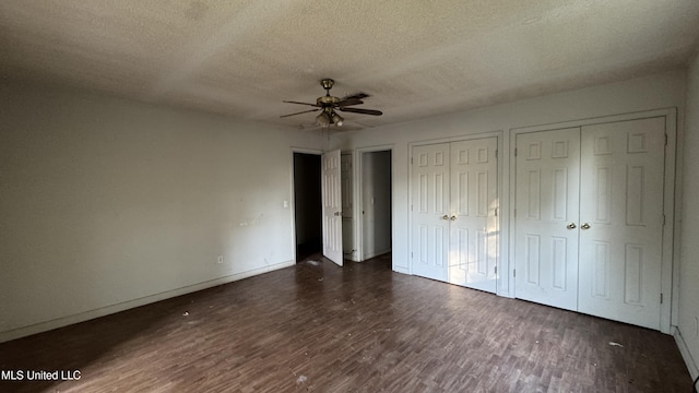 unfurnished bedroom featuring a textured ceiling, dark hardwood / wood-style flooring, ceiling fan, and multiple closets