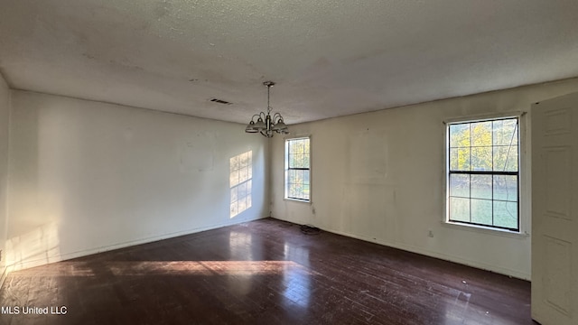 spare room featuring dark hardwood / wood-style flooring, plenty of natural light, a textured ceiling, and an inviting chandelier