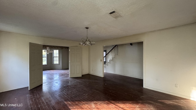 spare room featuring a textured ceiling, dark hardwood / wood-style flooring, and an inviting chandelier