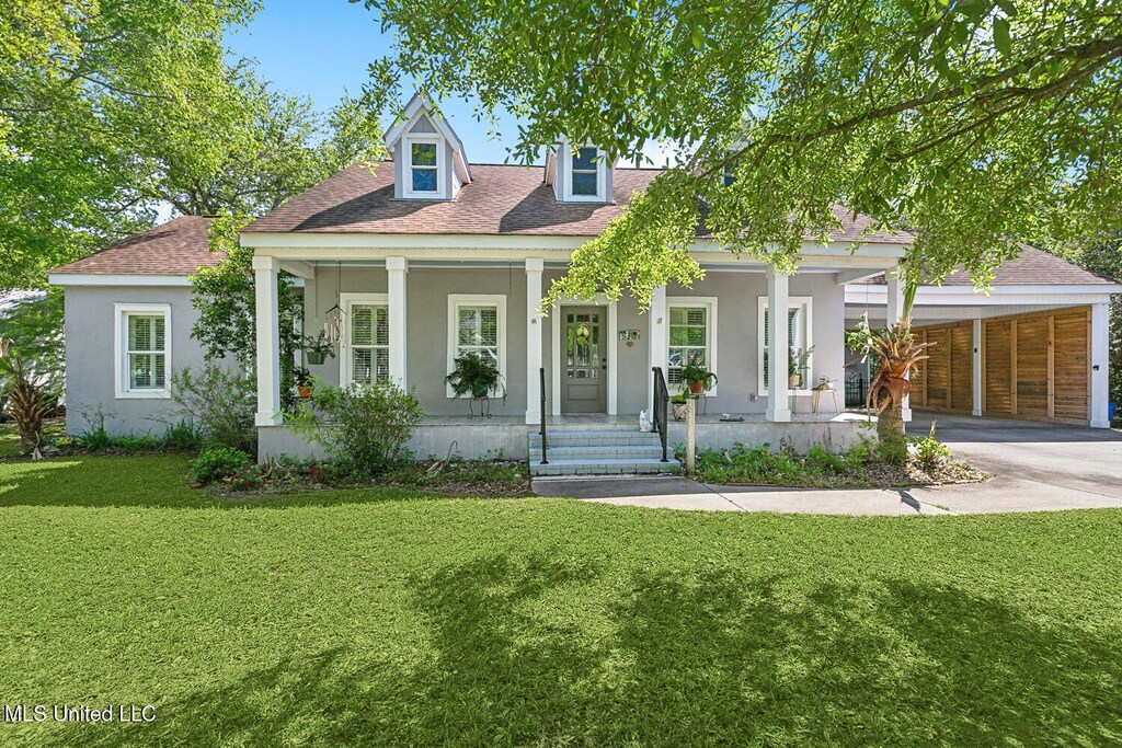 210 Bay Oaks Dr, Bay Saint Louis, MS 39520 - view of front of house with a front yard, a shingled roof, a porch, stucco siding, and driveway