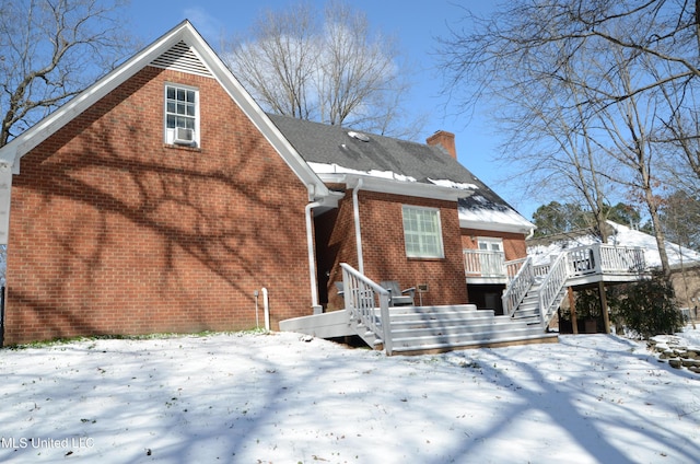 snow covered back of property featuring brick siding, stairs, a chimney, and a wooden deck