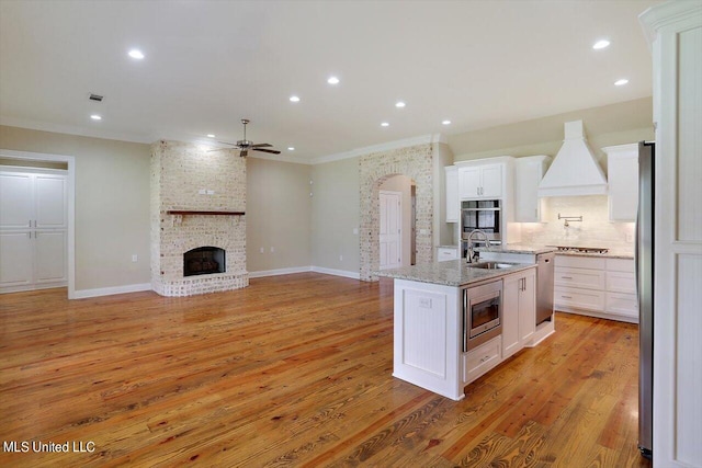 kitchen with an island with sink, stainless steel appliances, sink, light wood-type flooring, and white cabinetry