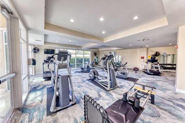 gym with a tray ceiling and carpet flooring