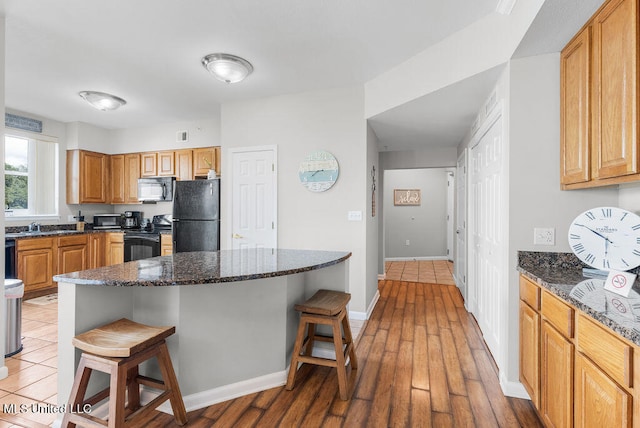 kitchen featuring black appliances, sink, a kitchen bar, dark stone countertops, and dark hardwood / wood-style floors