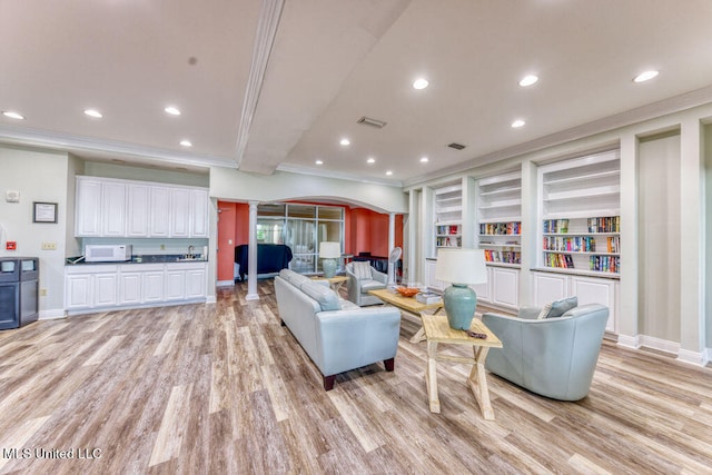 living room with light hardwood / wood-style floors, crown molding, ornate columns, and built in shelves