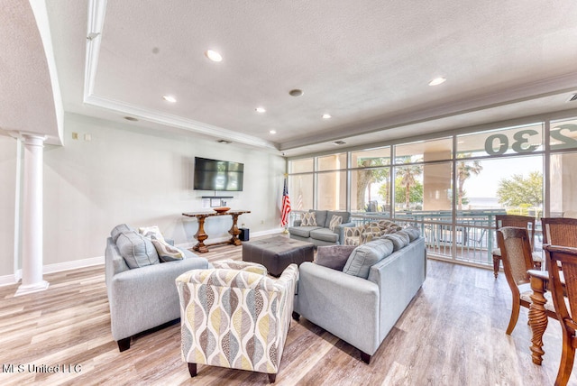 living room with light hardwood / wood-style floors, a textured ceiling, a tray ceiling, and ornate columns