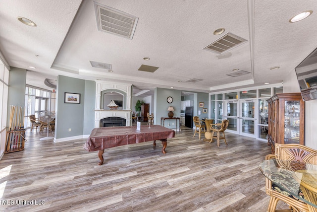 recreation room featuring french doors, a raised ceiling, a textured ceiling, and light hardwood / wood-style flooring