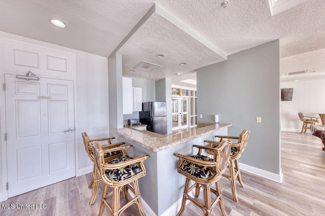 kitchen featuring light hardwood / wood-style floors, a textured ceiling, kitchen peninsula, and black fridge