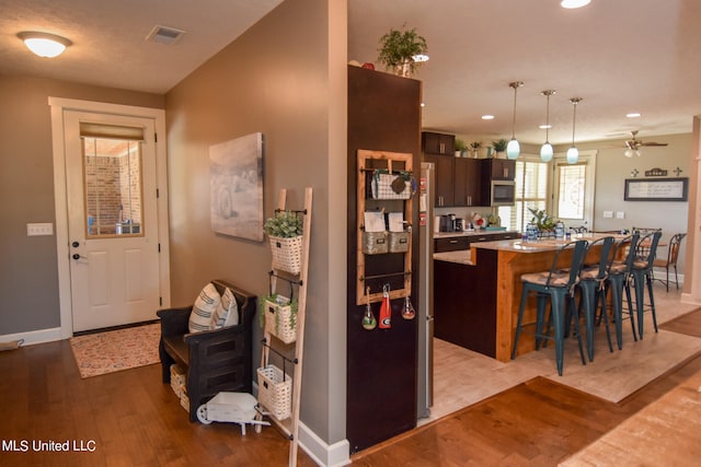 kitchen featuring ceiling fan, a kitchen island, a breakfast bar, light hardwood / wood-style floors, and dark brown cabinetry