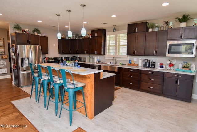 kitchen featuring a kitchen island, appliances with stainless steel finishes, a kitchen bar, and dark brown cabinets