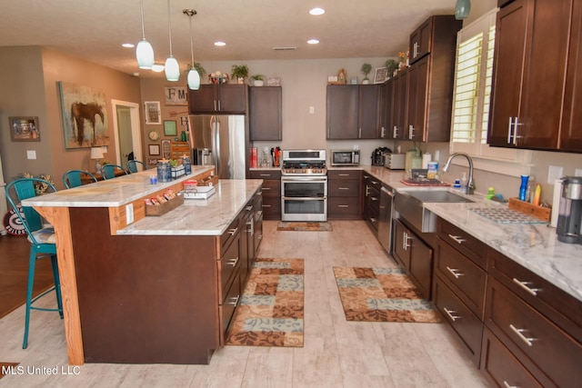 kitchen featuring appliances with stainless steel finishes, sink, light wood-type flooring, a kitchen bar, and a center island