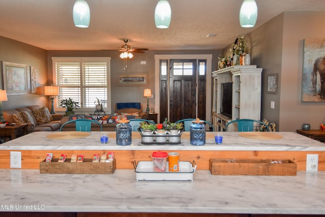 kitchen featuring ceiling fan, light stone countertops, a textured ceiling, and hanging light fixtures