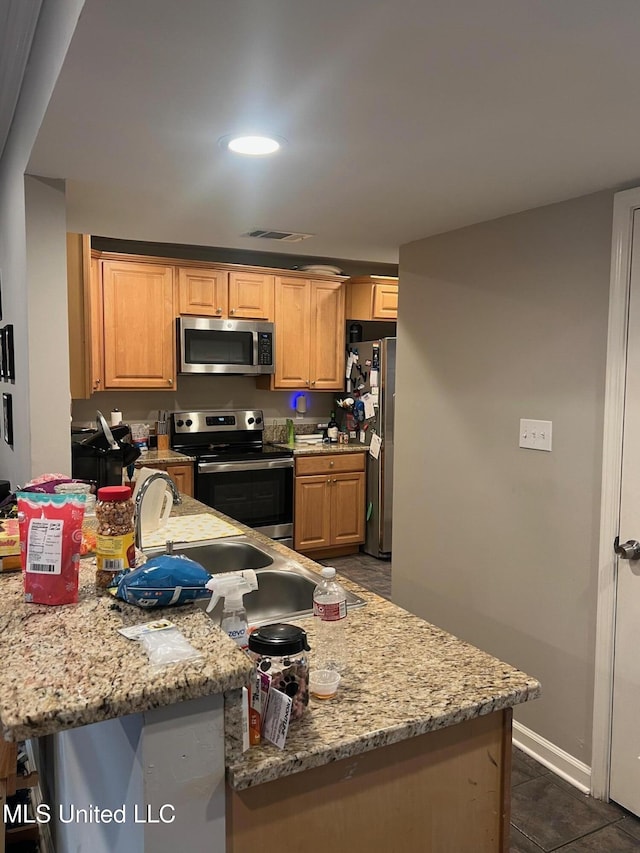 kitchen featuring stainless steel appliances, light stone countertops, light brown cabinets, and dark tile patterned flooring