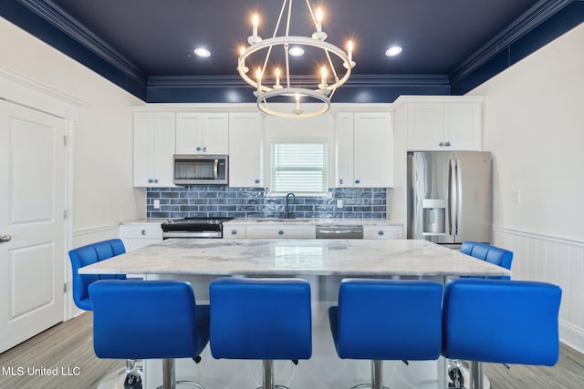 kitchen with appliances with stainless steel finishes, decorative light fixtures, light hardwood / wood-style floors, white cabinets, and a center island