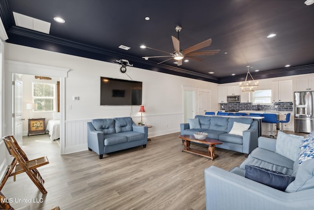 living room with a wealth of natural light, ceiling fan with notable chandelier, light wood-type flooring, and ornamental molding