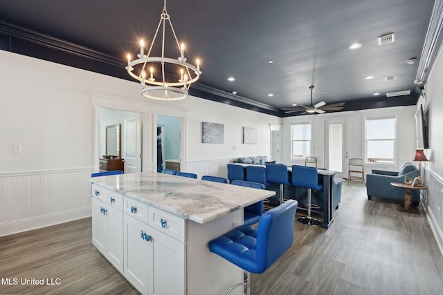 kitchen featuring a breakfast bar, ornamental molding, a center island, white cabinets, and dark wood-type flooring