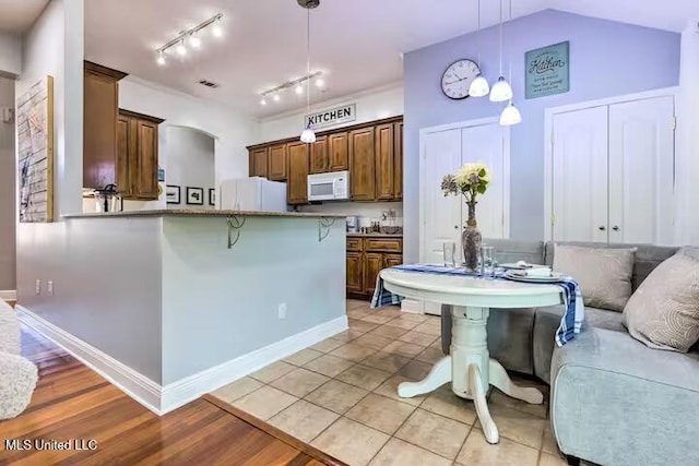 kitchen with hanging light fixtures, a breakfast bar area, white appliances, vaulted ceiling, and kitchen peninsula