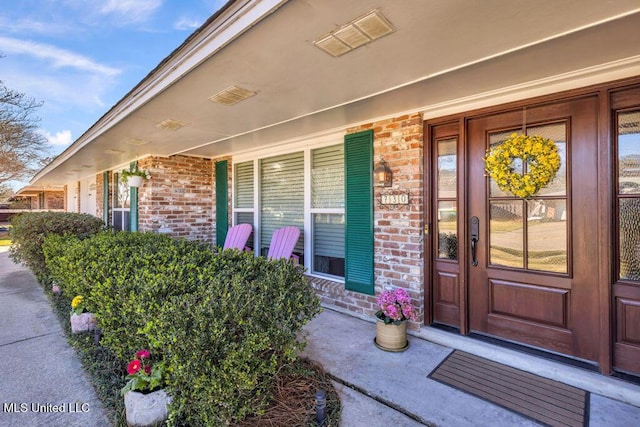 entrance to property featuring covered porch, brick siding, and visible vents