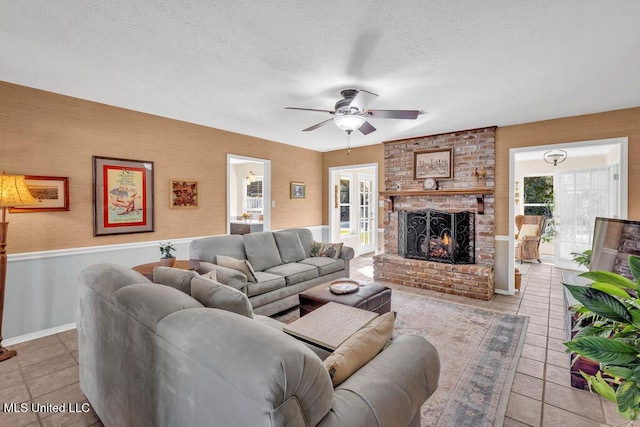 living area with a textured ceiling, light tile patterned flooring, a ceiling fan, and a brick fireplace